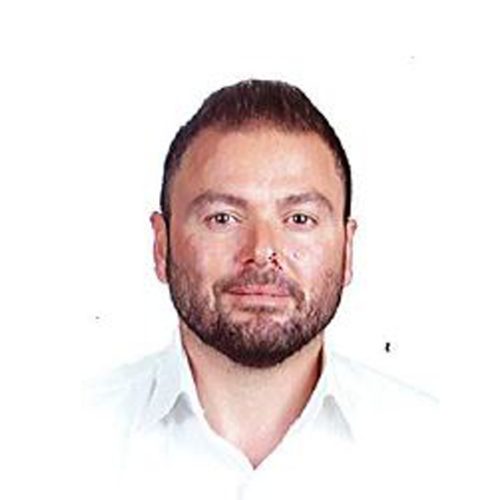 A headshot of a man with short dark hair, a trimmed beard and mustache, wearing a white collared shirt. He is looking directly at the camera against a plain white background.